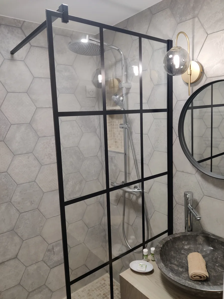 Douche à l’italienne fermée par une verrière noire, carrelage hexagonal