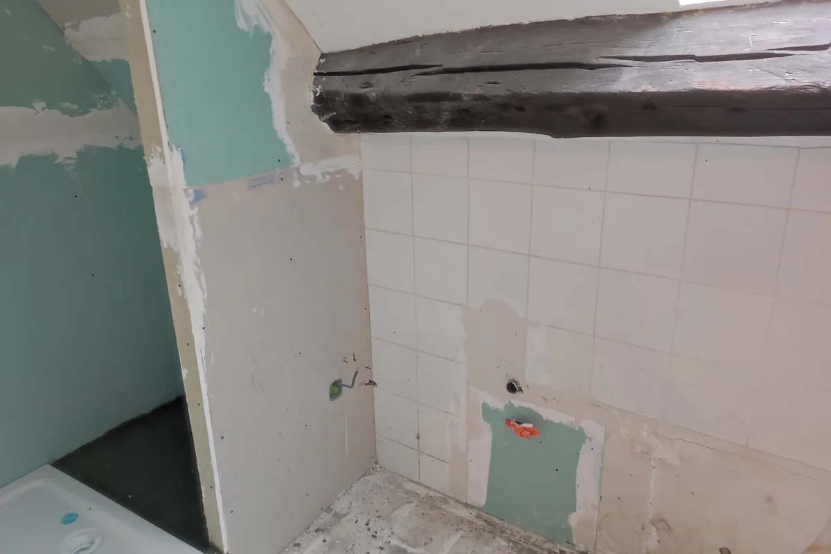 La salle de bain avant travaux : sanitaires déposés, ancien carrelage et poutre brute