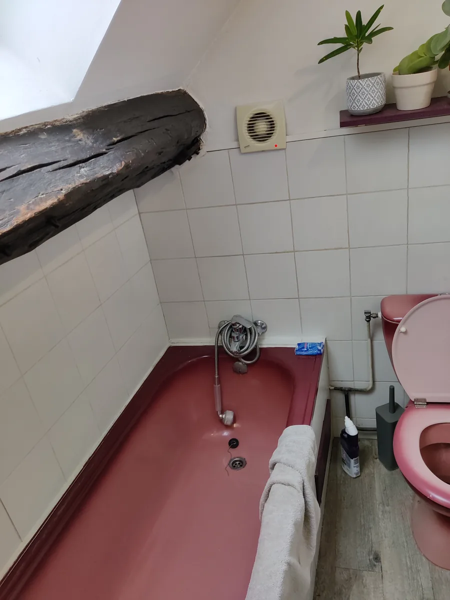 La salle de bain d'origine : baignoire et sanitaires roses sous la poutre